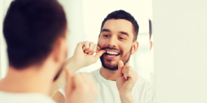 'man flossing teeth in mirror'